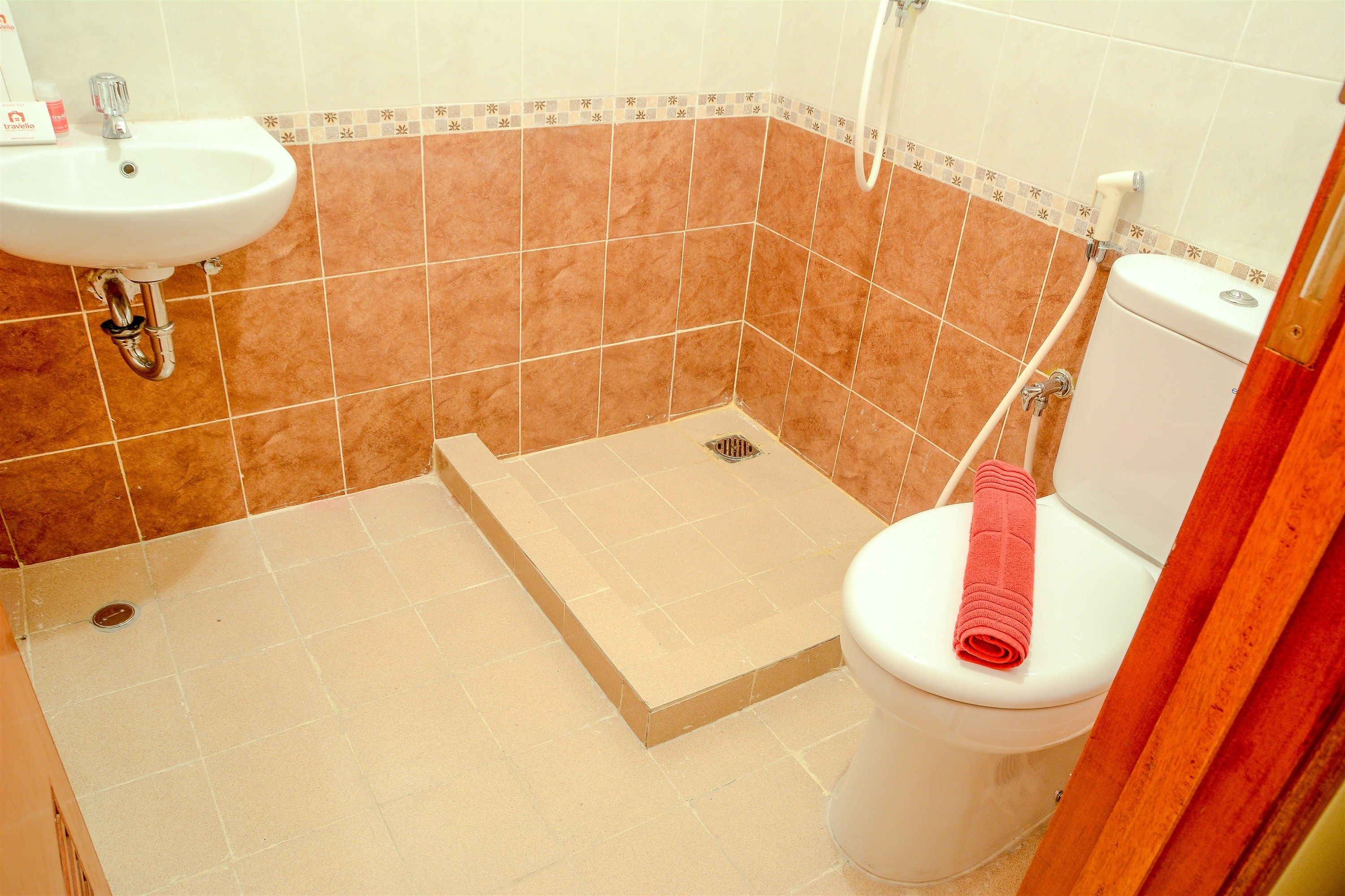 A bathroom with a sink, toilet, shower, and a small step leading to the shower.