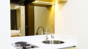 A modern kitchen with a stainless steel sink, a built-in stove, and a mirror above the counter. - Modern Style The Oasis Studio Apartment with Comfortable Sofa (Cikarang)