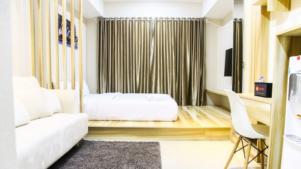A modern hotel room with a bed, a desk, a chair, and a TV. - Modern Style The Oasis Studio Apartment with Comfortable Sofa (Cikarang)