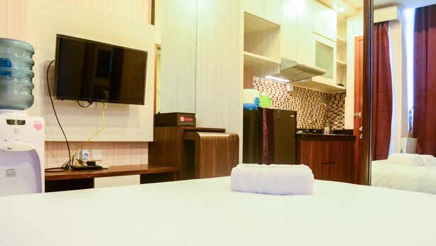 A hotel room with a bed, a TV mounted on the wall, a water dispenser, and a small kitchenette area.