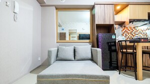 A compact living space with a sofa bed, a kitchen area with a checkered backsplash, and a dining table with chairs. - Classic 2BR Bassura City Apartment (Jakarta)