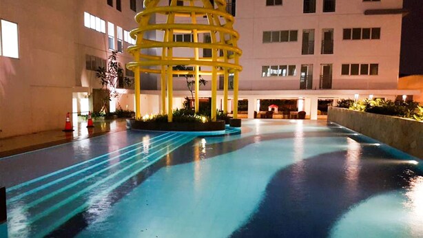 A pool area with a yellow structure in the center, surrounded by a building with multiple windows. - Classic 2BR Bassura City Apartment (Jakarta)
