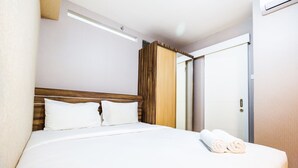 A hotel room with a large bed, wooden headboard, white linens, and a set of towels on the bed. - Classic 2BR Bassura City Apartment (Jakarta)