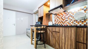 A compact kitchen with wooden cabinets, a tiled backsplash, and a small dining area with stools. - Classic 2BR Bassura City Apartment (Jakarta)