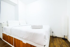 A white bed with a wooden headboard, a bedside table, and a lamp. - Modern And Comfy 3BR Bassura City Apartment (Jakarta)