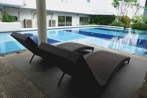 A swimming pool with lounge chairs and a white building in the background. - Modern And Comfy 3BR Bassura City Apartment (Jakarta)
