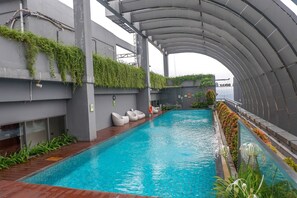 A swimming pool with a curved roof, surrounded by greenery and seating areas. - 2BR Cozy and Modern L'Avenue Apartment (Jakarta)
