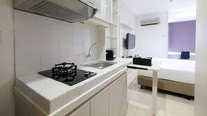 Una cocina moderna con estufa a gas, lavamanos y microondas. Se ve una cama con un televisor al fondo.