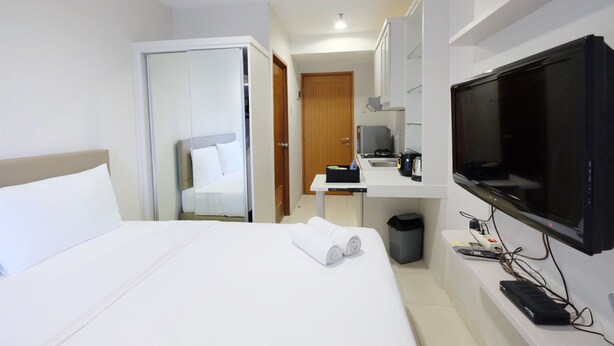 Habitación de hotel con cama, televisor, escritorio con computadora y baño visible a través de una puerta abierta.