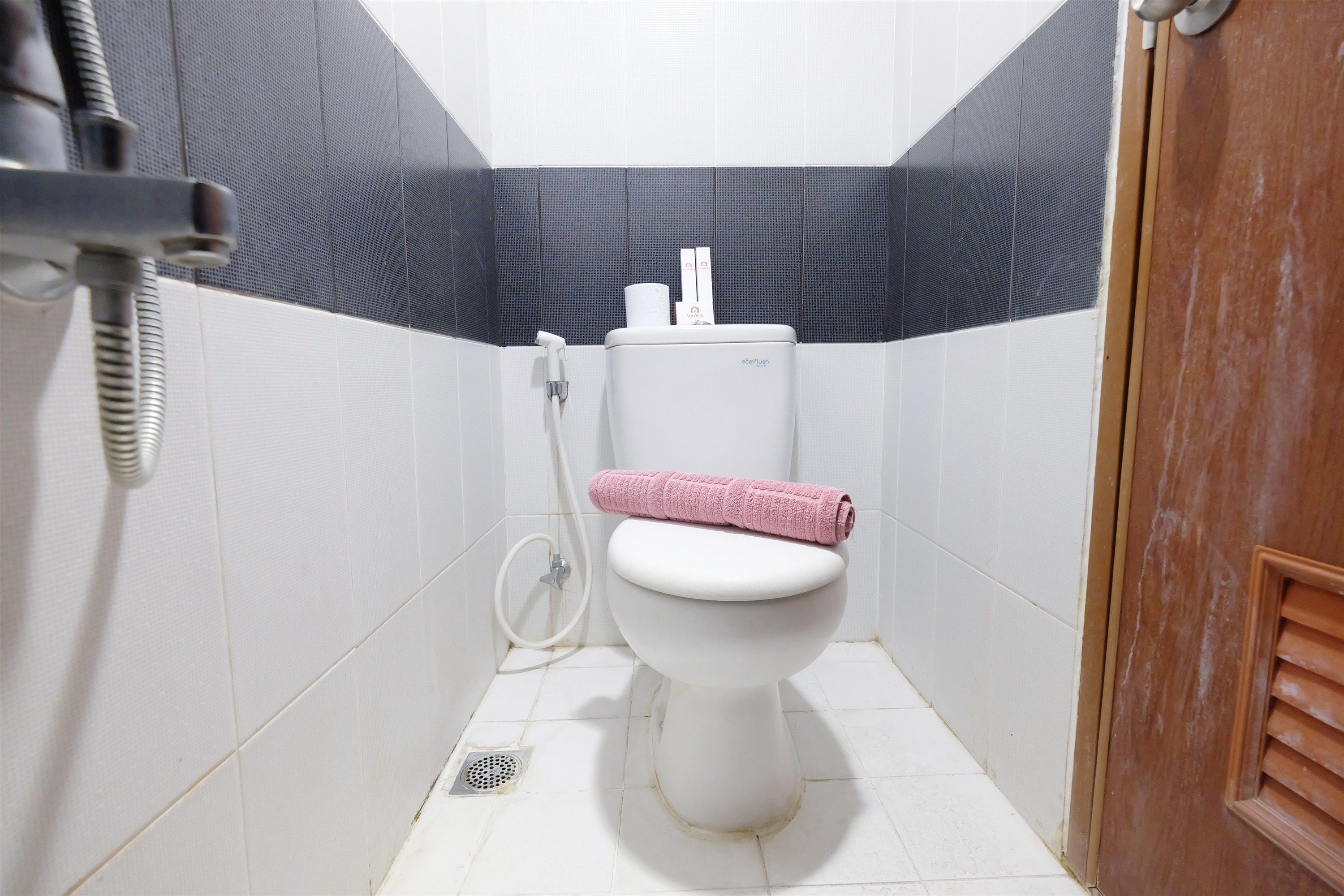 Un baño pequeño y limpio con un inodoro blanco, un cabezal de ducha y una toalla rosa sobre el asiento.