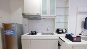 Cocina compacta con refrigerador de acero inoxidable, estufa integrada, un lavabo y microondas. Hay repisas de vidrio sobre el lavabo y una cafetera pequeña en la encimera.