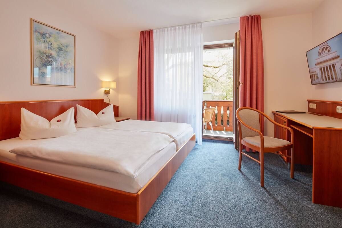 A hotel room with a double bed, a desk, a chair, a lamp, and a painting.
