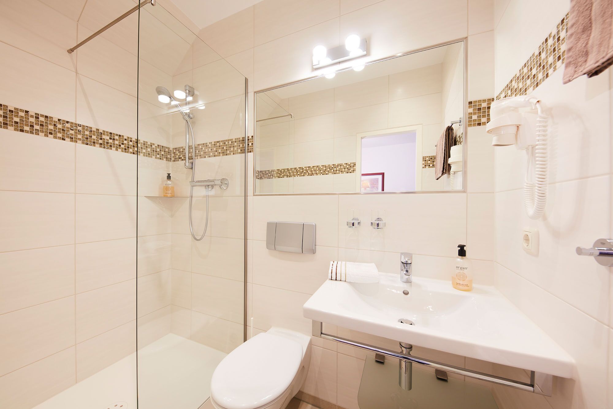 A modern bathroom with a glass-enclosed shower, a white sink with a mirror above it, and a toilet.