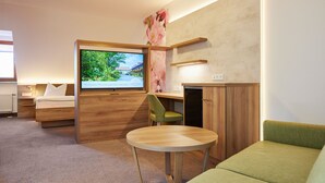 A modern hotel room with a bed, a TV, a desk, and a green sofa. - Hotel garni Sonnenhof (Moritzburg)
