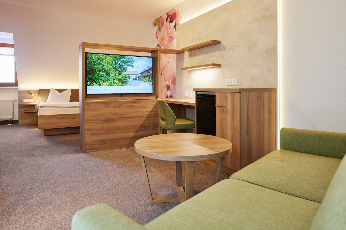 A modern hotel room with a bed, a TV, a desk, and a green sofa.