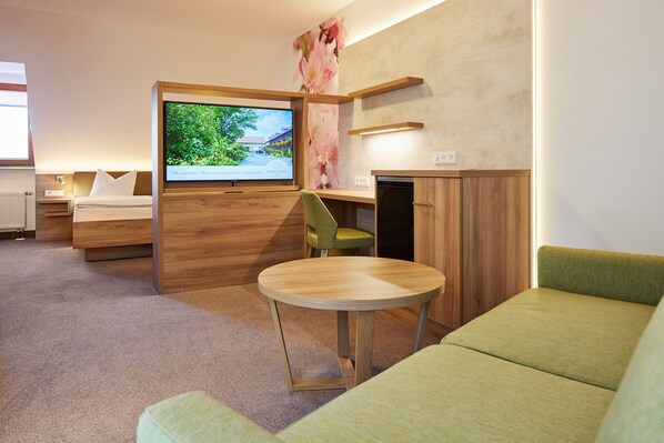 Quarto de hotel moderno com cama, televisão, escrivaninha e sofá verde.