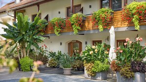 A building with a balcony adorned with flowers and plants, potted plants in the foreground, and a door with an arched entrance. - Hotel garni Sonnenhof (Moritzburg)