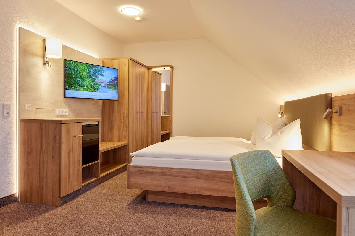 A hotel room with a bed, a desk, a chair, a TV, and wooden cabinets.