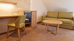 A compact living space with a kitchenette, a green sofa, a wooden chair, and a small round table. - Hotel garni Sonnenhof (Moritzburg)