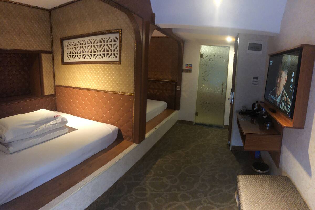 A hotel room with a bed, a small desk, a television, and a door leading to a bathroom.