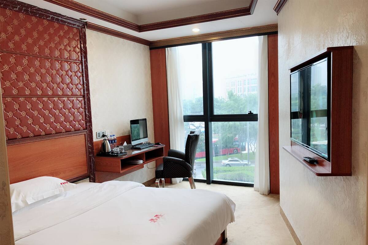 A hotel room with a large bed, a desk with a computer, and a TV.
