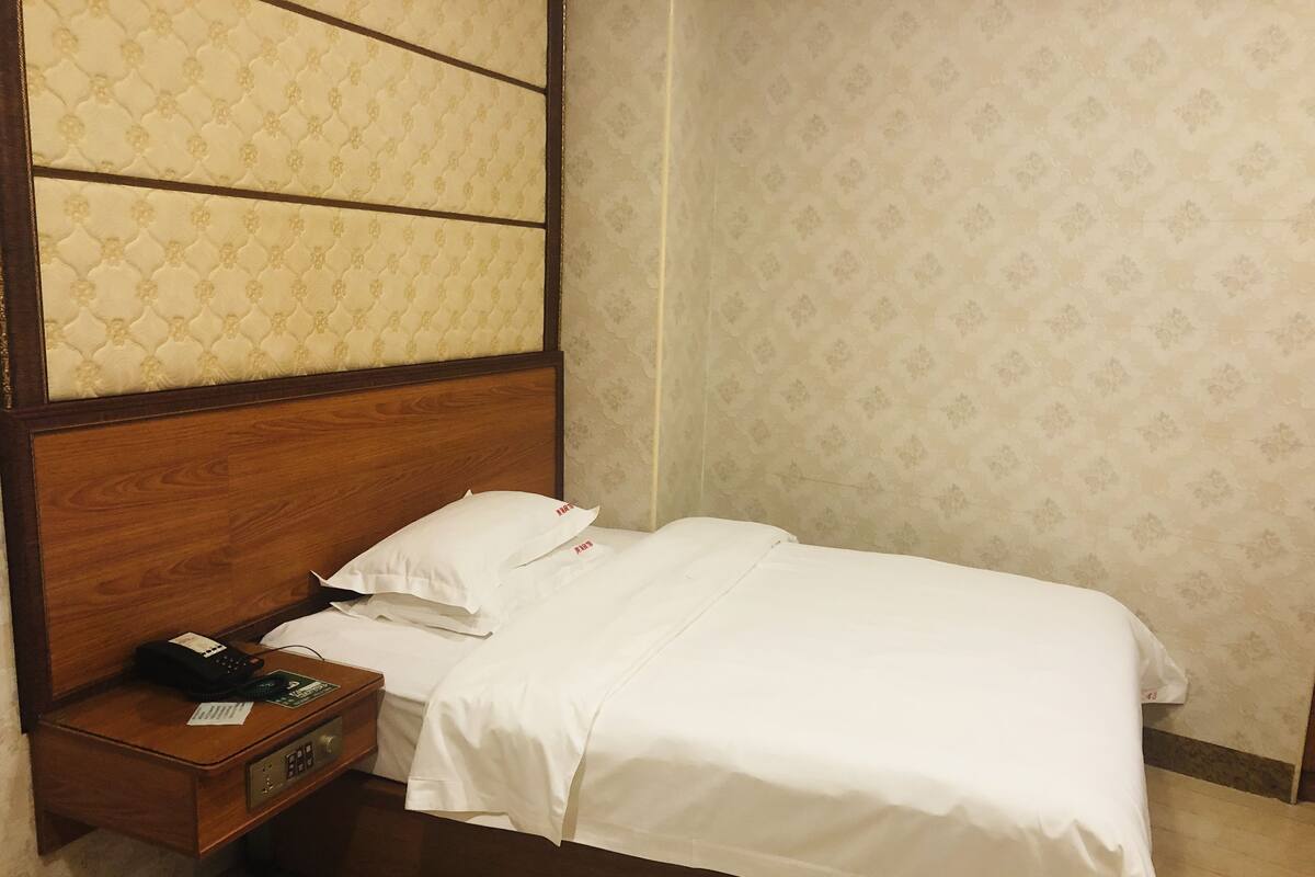 A neatly made bed with white linens, a wooden headboard, and a bedside table with a phone and a small item on it.