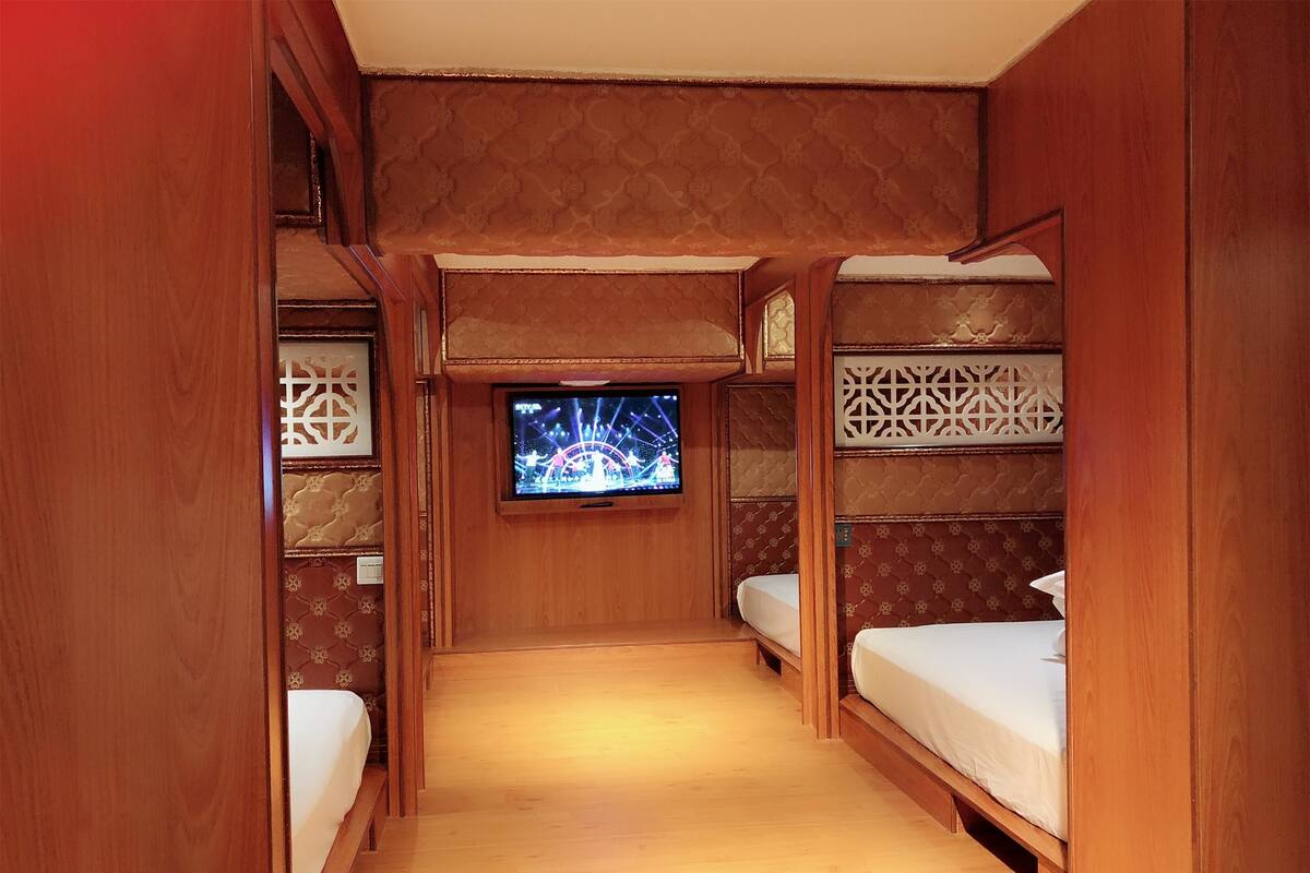 A narrow, wooden-paneled room with bunk beds and a television screen displaying a show.