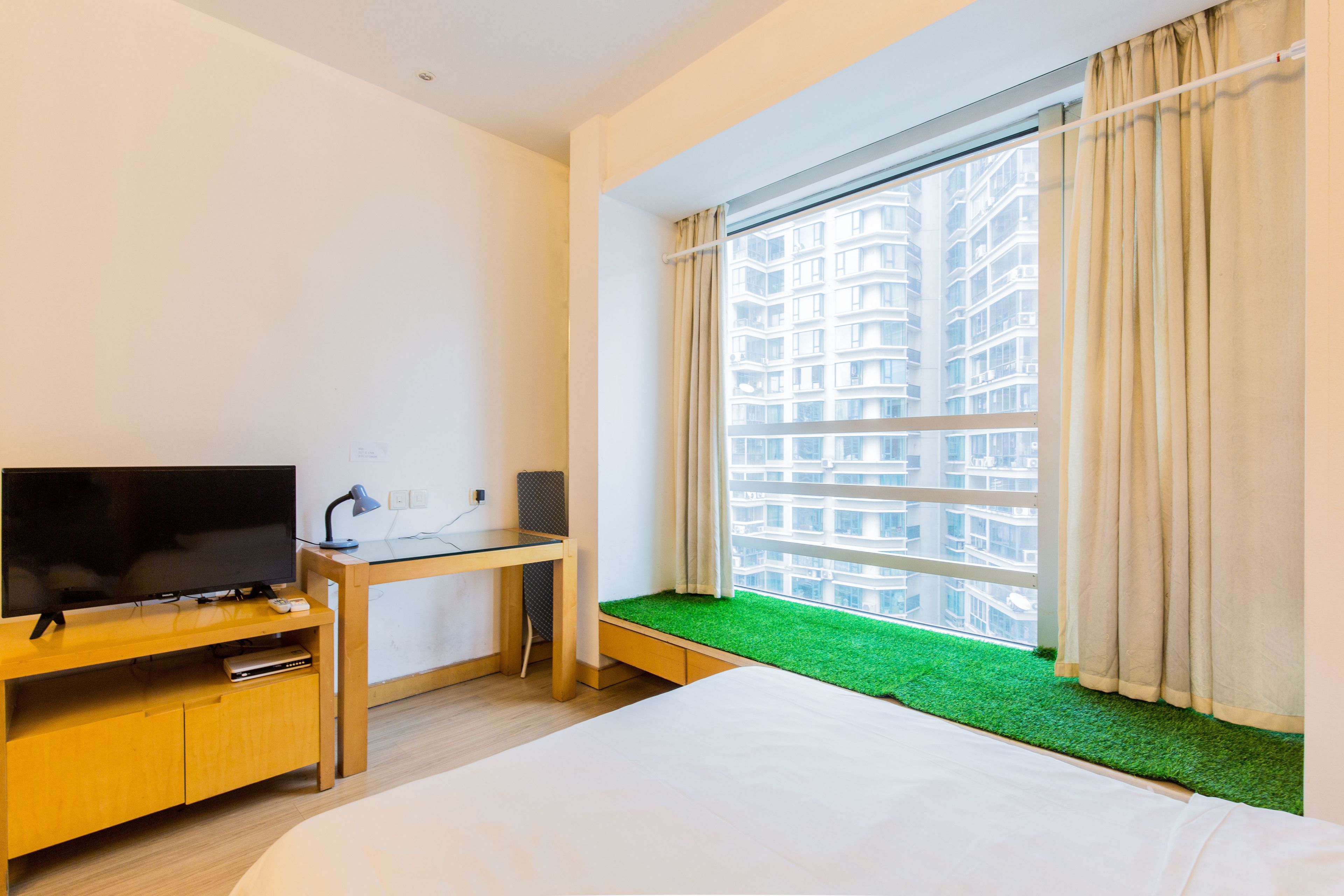 Een hotelkamer met een bed, een televisie op een houten standaard, een bureau en een raam met uitzicht op een gebouw.