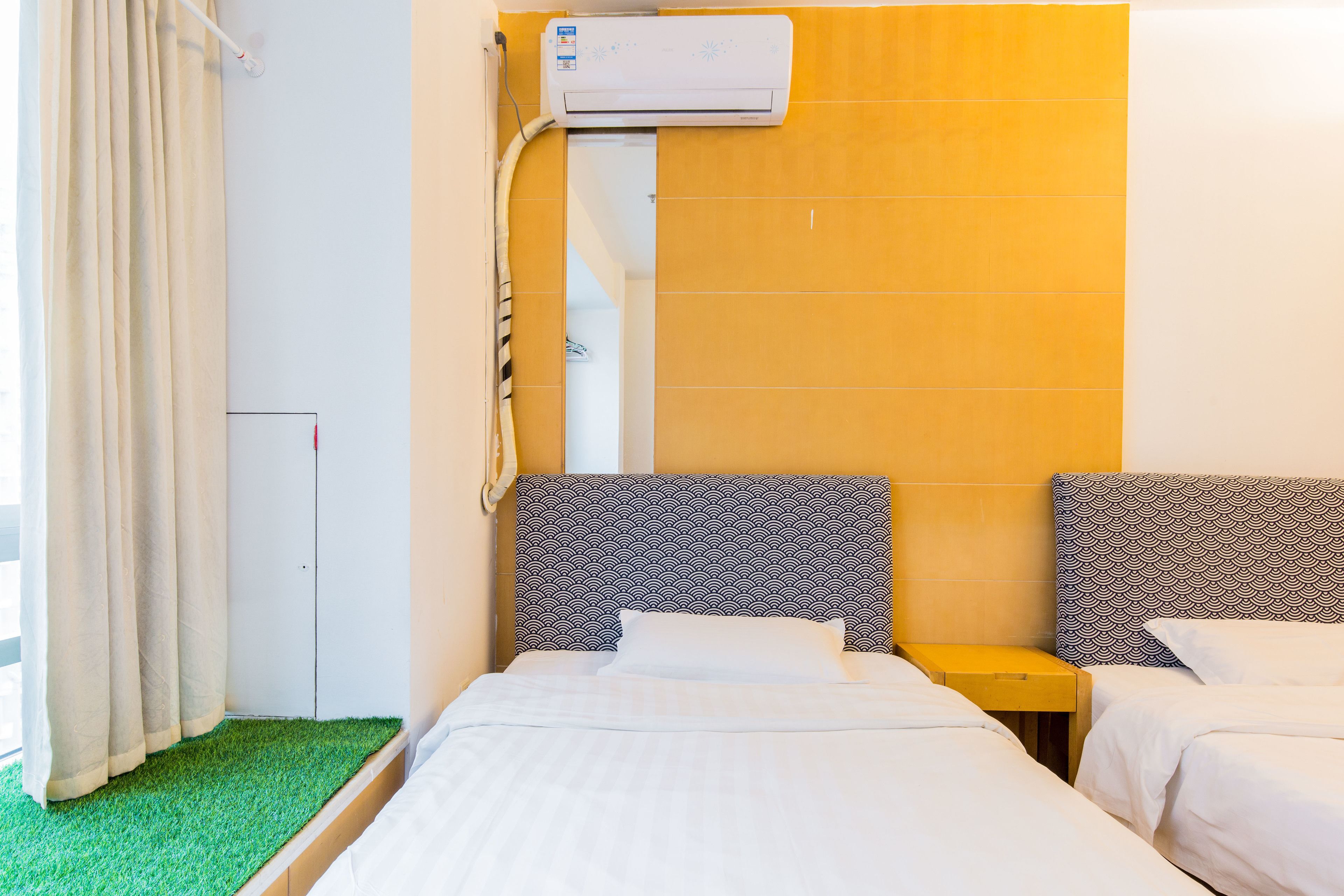 A hotel room with two beds, a wall-mounted air conditioner, and a green artificial grass floor.