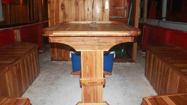 Una mesa de billar de madera en una sala con paredes rojas y bancos de madera.