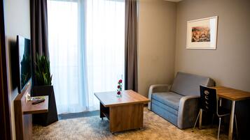 Habitación de hotel con sofá, una pequeña mesa de madera, televisor y una planta en maceta.