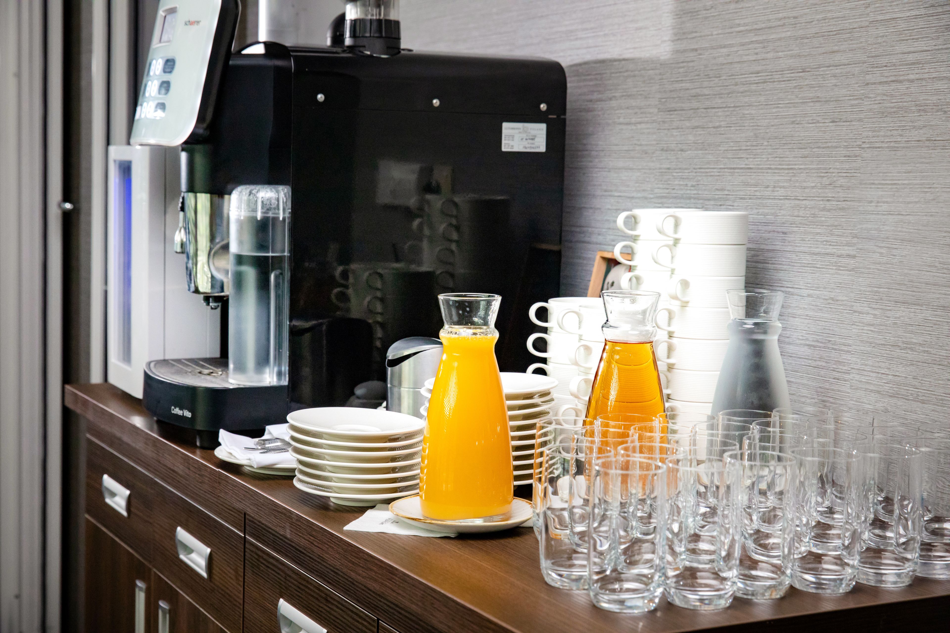 A coffee machine, stacked plates, and clear glasses on a wooden counter.