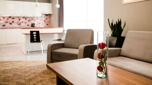 A modern living room with a wooden coffee table, a glass vase with red roses, a beige sofa, and a kitchen in the background.