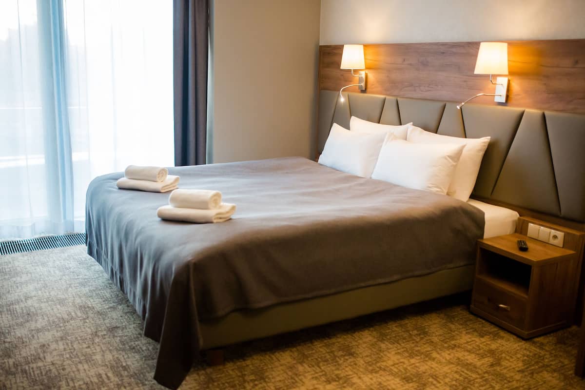 A hotel room with a large bed, two bedside lamps, a nightstand, and a window with curtains.