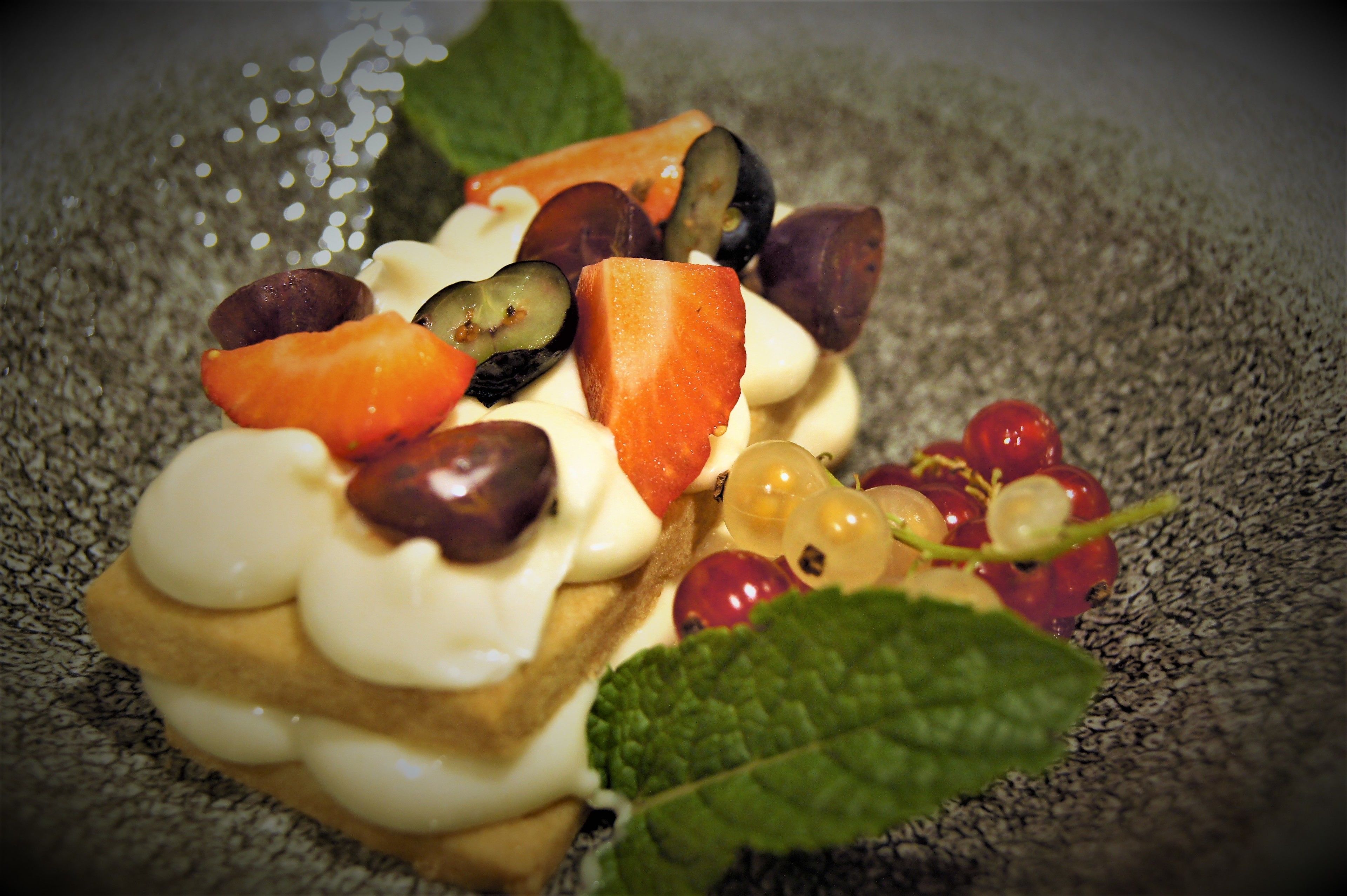 A dessert with various fruits and a leaf on a textured plate.