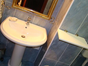 Une salle de bain avec un lavabo blanc, un miroir et une petite étagère.
