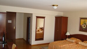 Habitación de hotel con cama, escritorio, silla, armario y un cuadro en la pared.