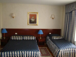 Une chambre d’hôtel avec deux lits, chacun doté de draps à rayures, deux lampes de chevet, une œuvre d’art florale encadrée accrochée au mur et un rideau à rayures.