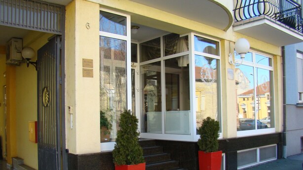 Fachada de hotel amarilla, con grandes ventanales y un balcón con barandilla de metal.