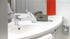 A bathroom with a white sink, a mirror, a toothbrush holder, and a towel. - ibis Landshut City (Landshut)