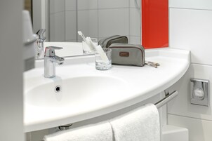 Un baño con lavamanos blanco, espejo, porta cepillos de dientes y toalla.