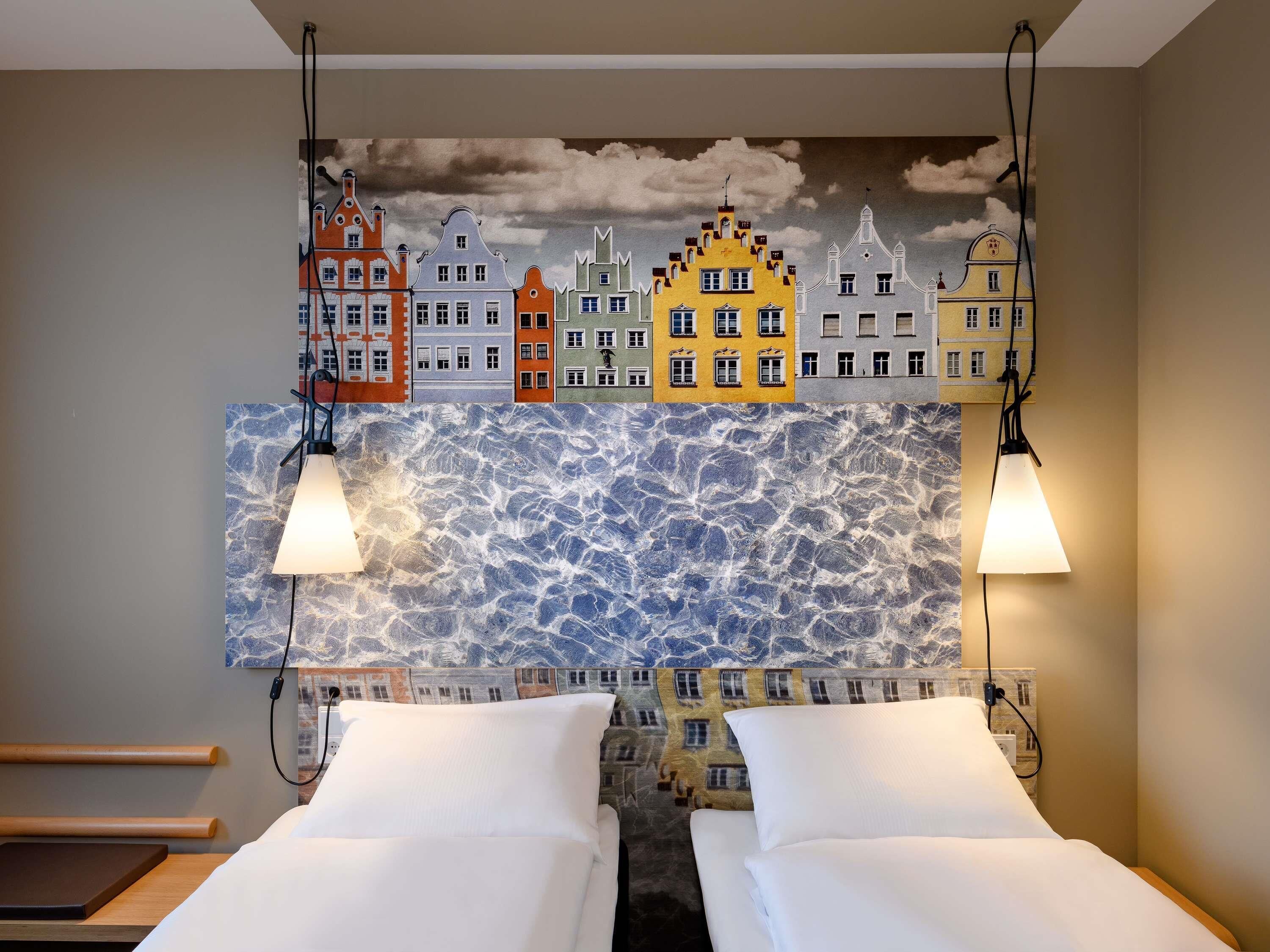 A hotel room with two beds, a cityscape mural, and a textured wall.