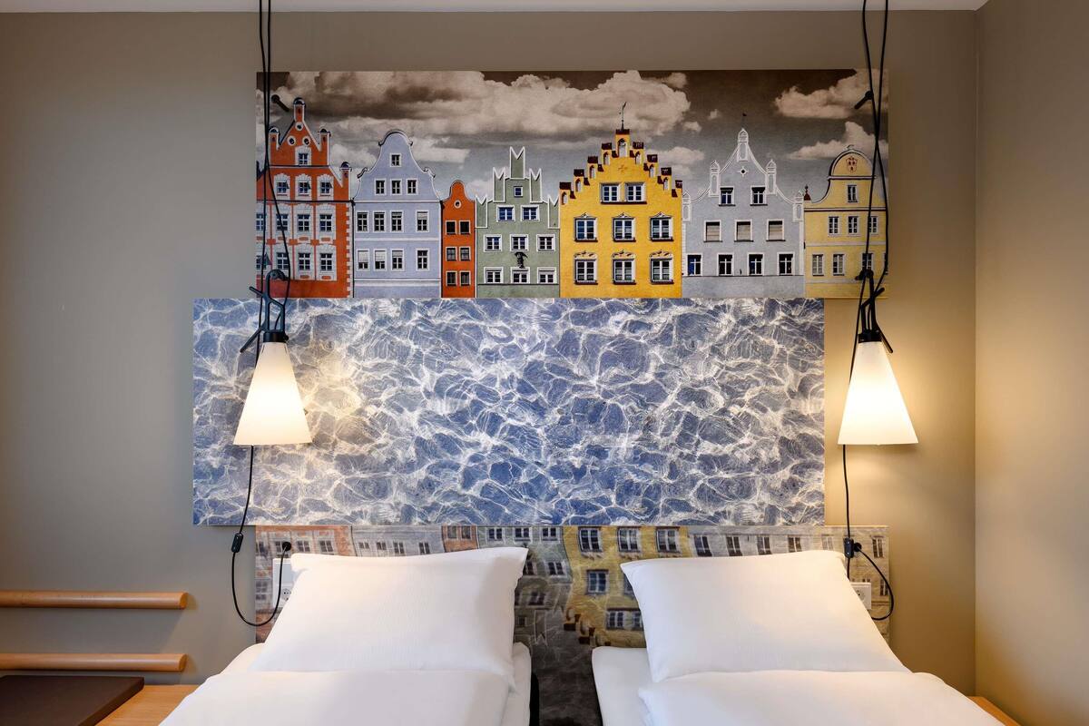 A hotel room with two beds, a cityscape mural, and a textured wall.