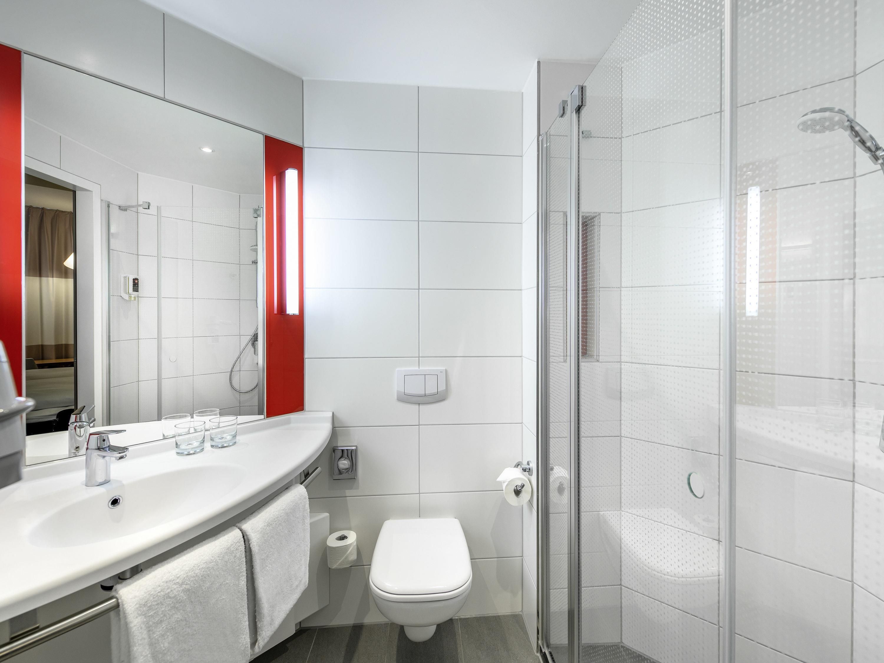 Ein modernes Badezimmer mit großem Spiegel, Waschbecken in Weiß, Toilette und einer Duschkabine.