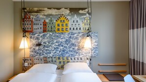 Une chambre d’hôtel avec deux lits, une fresque représentant un paysage urbain et une vue sur la mer.