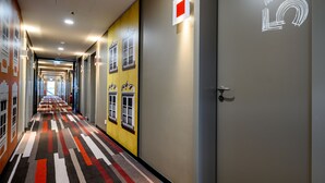 A hotel corridor with a patterned carpet, doors with window designs, and a lighted exit sign. - ibis Landshut City (Landshut)