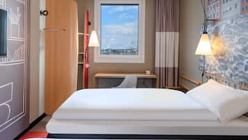 Una camera d'albergo con un letto, una scrivania, una finestra vista, una lampada e una porta.