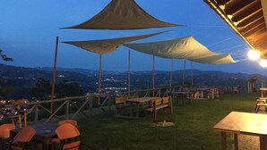 An outdoor seating area with tables and chairs, shaded by large triangular canopies, overlooking a cityscape at dusk. - Agriturismo Lo Scoiattolo (Montorio al Vomano)