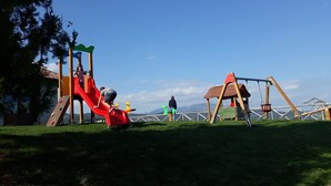 A playground with a red slide and swings, set against a backdrop of mountains and clear sky. - Agriturismo Lo Scoiattolo (Montorio al Vomano)