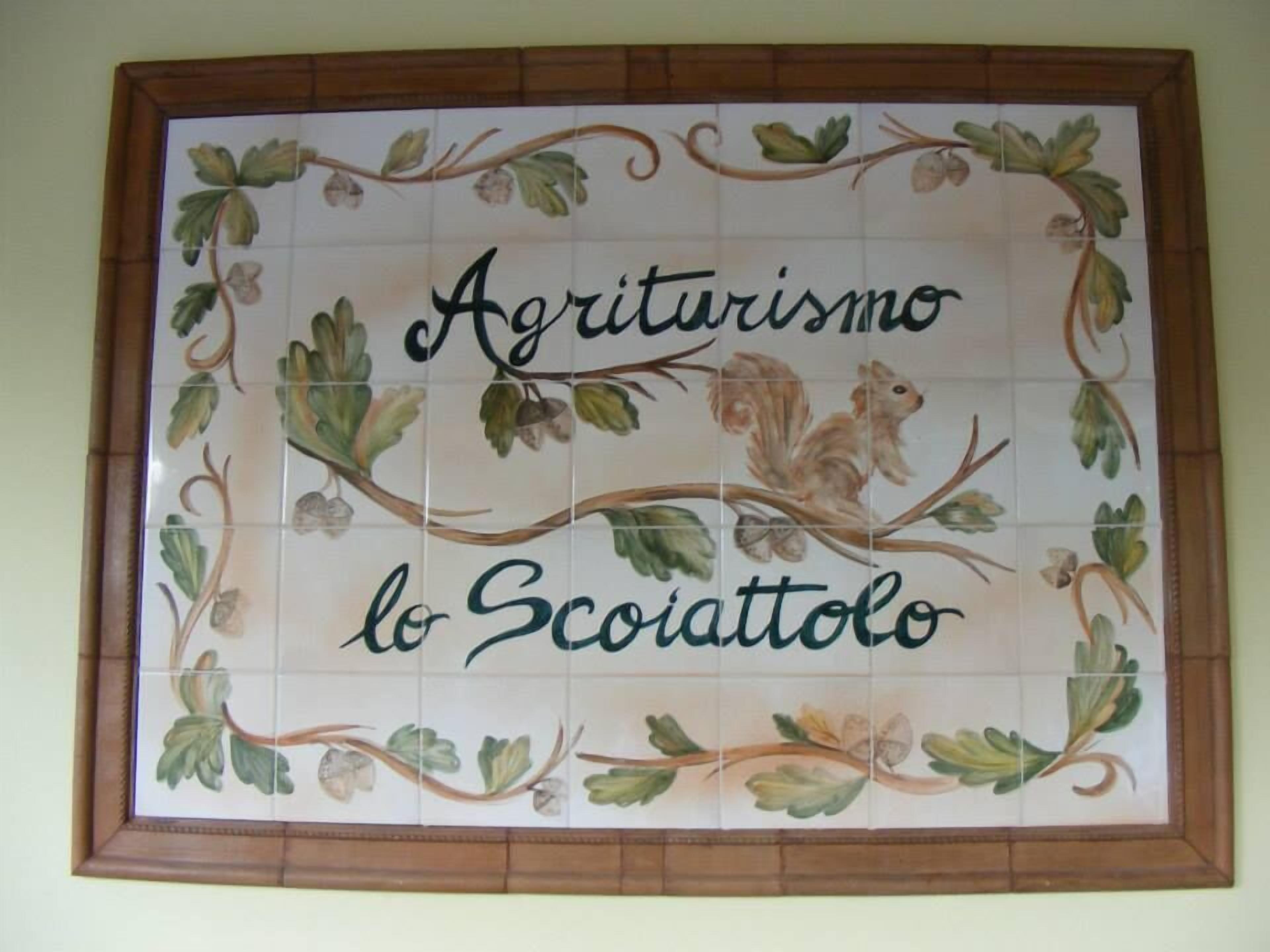 Una baldosa decorativa con el texto "Agriturismo lo Sciatto" rodeado de motivos con temática natural.